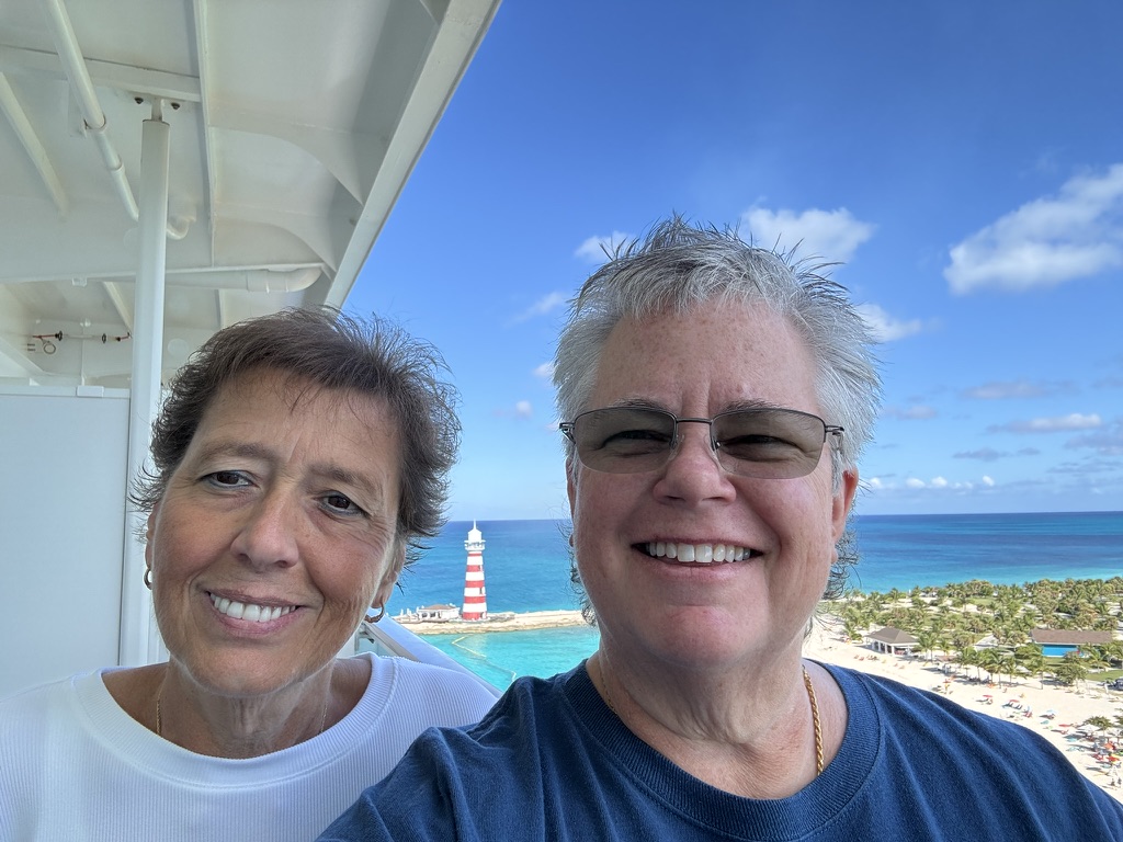 Anne Conrad and her wife Kathy smiling on a cruise ship deck with the Ocean Cay lighthouse behind them