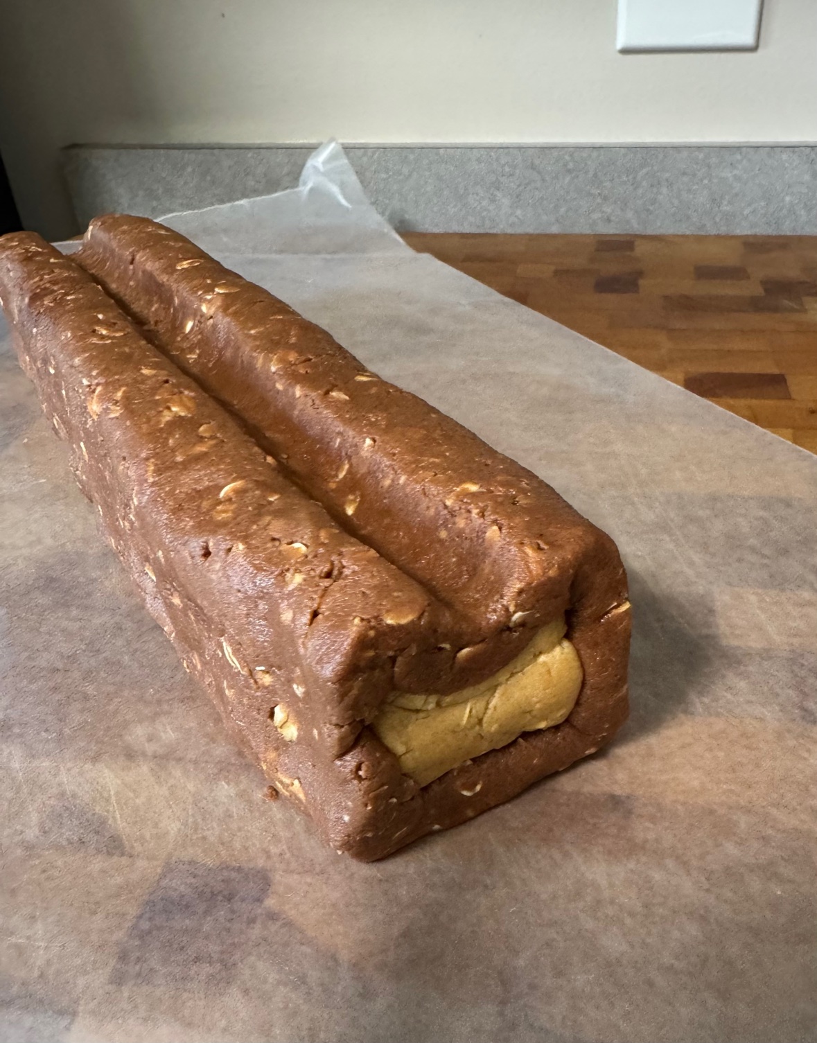 The owl cookie dough roll before chilling — chocolate dough wrapped around the peanut-butter roll, shaped into a square with an indent pressed down the top that will become the owl's ears